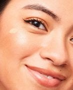 Smiling woman applying cream to her cheekbones