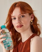 Picture of a red-haired model looking at the camera while holding a Garnier micellar water