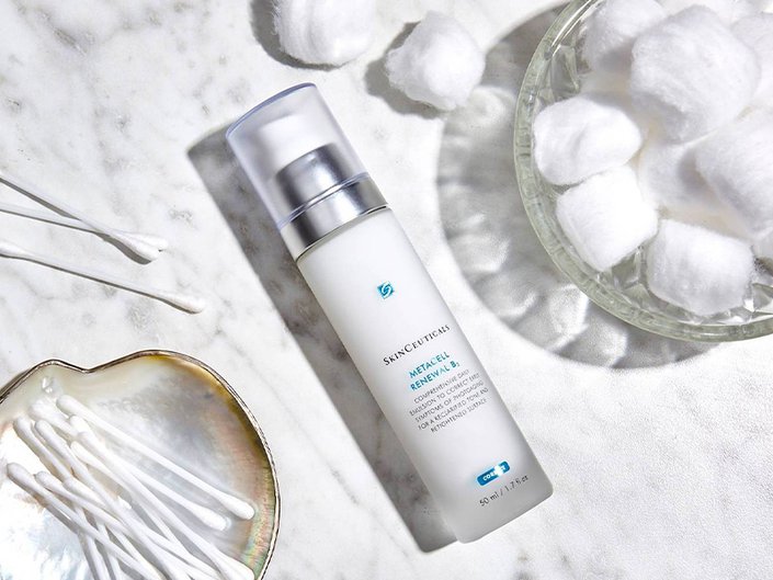 An overhead shot of the SkinCeuticals Metacell Renewal B3 lying on a bathroom countertop with a crystal bowl of cotton balls and a bowl of cotton swabs
