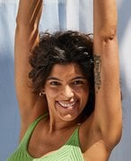 Picture of a model smiling, wearing a tank top with their arms raised above their head