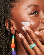 Black model smiling and applying sunscreen to her cheek 