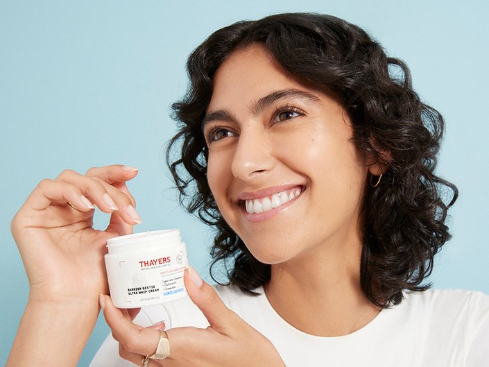 Person with dark curly hair smiling and holding a Thayers moisturizer