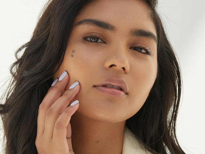 Close-up picture of a model looking into the camera and touching the side of their face