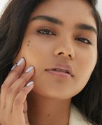 Close-up picture of a model looking into the camera and touching the side of their face