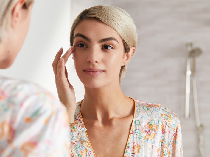 Person with a blonde pixie cut looking in the mirror touching her hand to her eyebrow