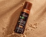 An image of the L'Oréal Paris Skincare Sublime Bronze Self-Tanning Water Mousse on top of sand