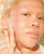 Picture of a blonde model with a septum piercing touching the side of their face