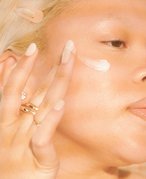 Person with bleached blonde hair swatching face cream into their cheek