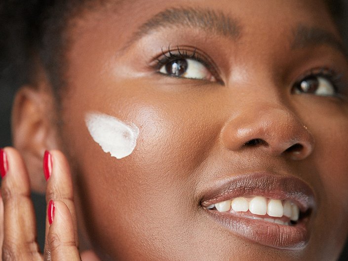 Picture of a person applying a white cream on their cheek.