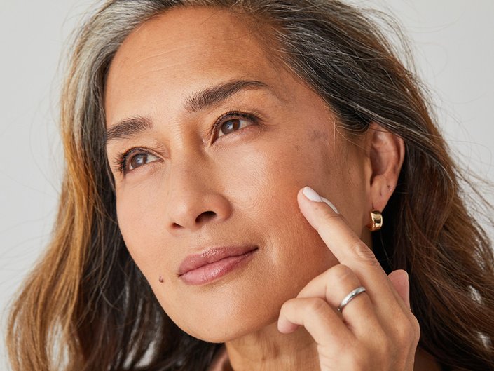 Close-up picture of a mature model looking to the side and touching their cheek