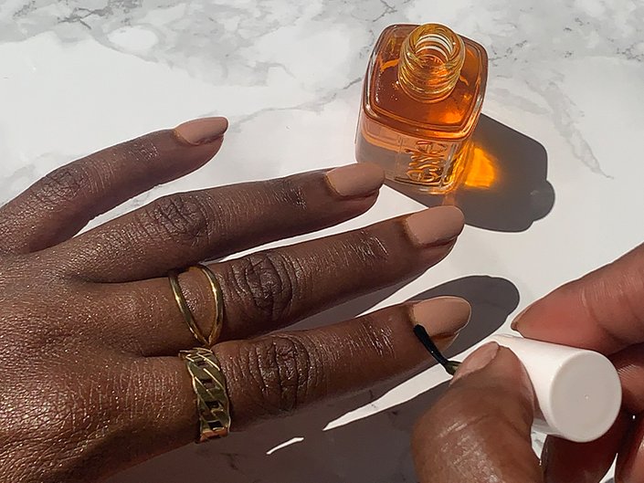 Person painting cuticle oil on nude nails