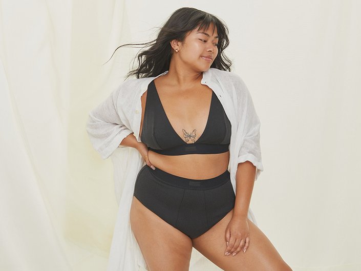 Person with long dark hair wearing a black bra and underwear with a white robe