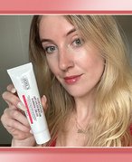 Picture of an editor holding the Kiehl’s Ultra Facial Advanced Repair Barrier Cream against a red graphic background