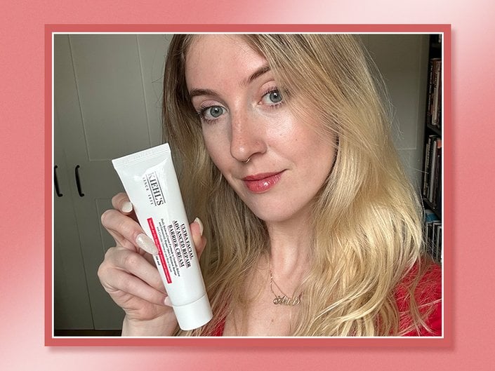 Picture of an editor holding the Kiehl’s Ultra Facial Advanced Repair Barrier Cream against a red graphic background