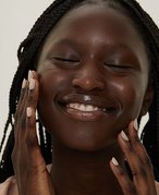 Close-up picture of a person smiling and touching the sides of their face