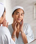 A person with clean, bare skin smiling and holding a towel up to their face 