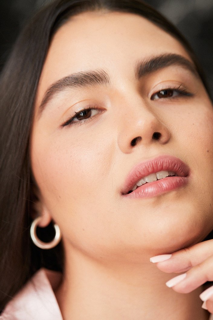 Person with dark hair looking at the camera holding their hand under their chin