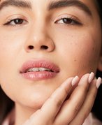 Person with dark hair looking at the camera and touching their hand to their jaw