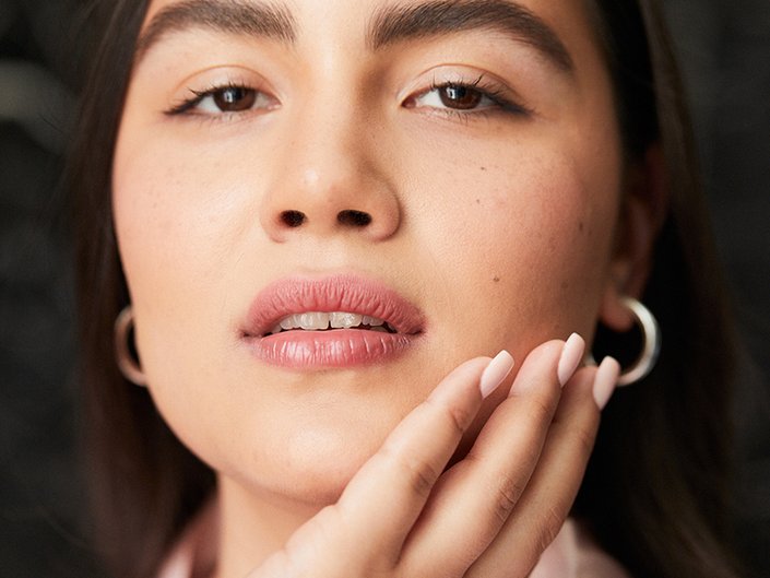 Person with dark hair looking at the camera and touching their hand to their jaw