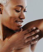 Person with short bleached hair looking down at their underarm and touching their hand to their underarm