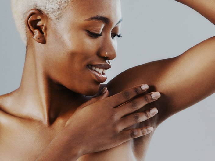 Person with short bleached hair looking down at their underarm and touching their hand to their underarm