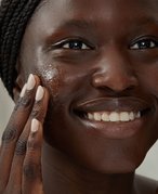 Picture of a model smiling and exfoliating their face