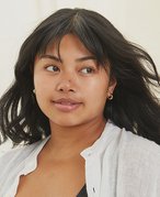 Person with long dark hair wearing a white shirt and natural makeup