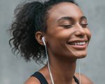 Person with dark hair pulled back in a ponytail smiling with their eyes closed and wearing earphones 